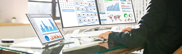 an image of three computer monitors with a man's hand on the keyboard