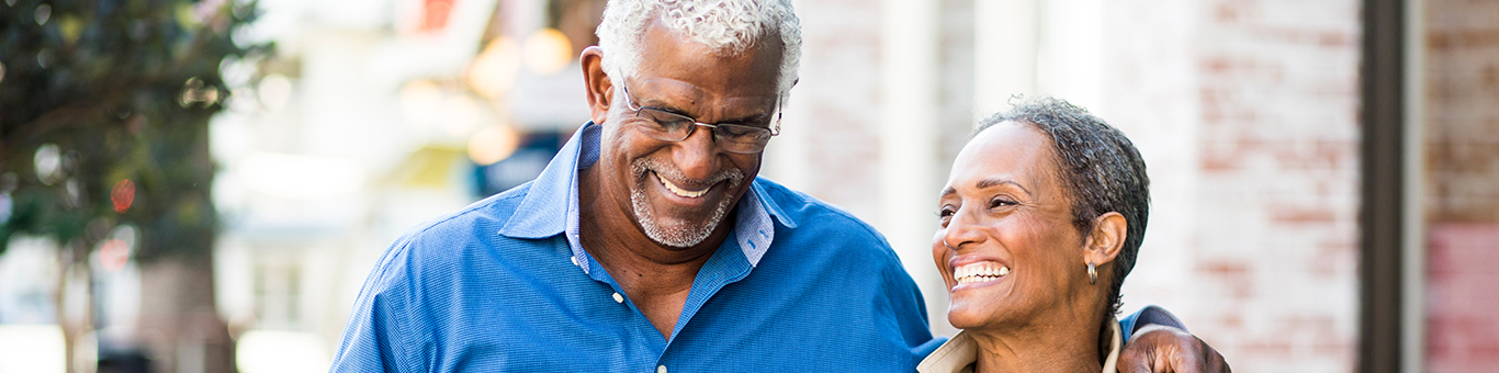 Older man and woman walking down a quiet city street, smiling and laughing