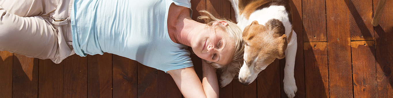 Content, relaxed woman laying on her back on a hardwood floor with her senior dog