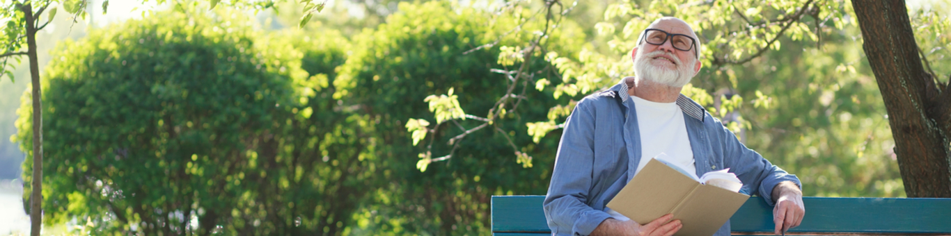 A man sitting on a park bench holding a book and looking pensive.