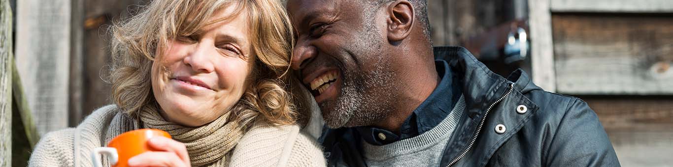 Middle-aged couple sitting on a rustic front porch, sipping coffee, laughing, and holding each other