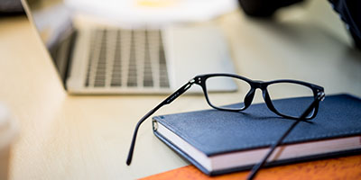 desk with a notebook, glasses, and laptop sitting on it