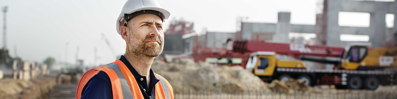 Utility worker looking intently across a work site, wearing a helmet and high-visibility vest