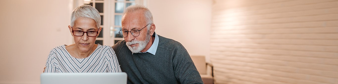 Older couple in a well-lit room, focused on an open laptop screen